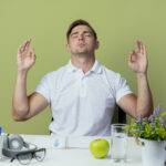 with-closed-eyes-young-handsome-male-student-sitting-desk-with-school-tools-showing-meditation-gesture-isolated-olive-green